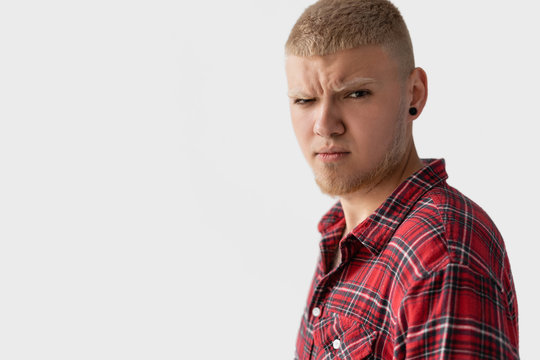 stylish young blond guy dressed in a red shirt stares intently at the camera.
