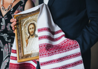A beautiful icon in a wooden frame with the image of Jesus Christ in the hands of the parents of the newlyweds. Wedding blessing. Photography, concept.