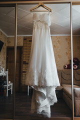 Wedding white long dress hanging on a hanger on a wardrobe with a mirror in a beautiful interior. Morning and preparation of the bride. Photography, concept.