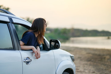 ํYoung Asian woman wearing sun glasses out of white SUV car window at the riverside, Travel car in vacation