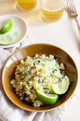 Cauliflower low-carb rice or couscous with chopped cilantro and lime in a brown bowl top view