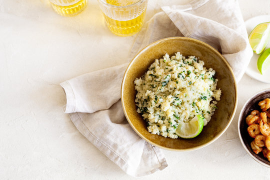 Cauliflower low-carb rice or couscous with chopped cilantro and lime in a brown bowl on white background with copy space