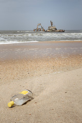 Obraz premium Alcohol bottle in the foreground with a shipwreck on the skeleton coast just outside Swakopmund, Namibia