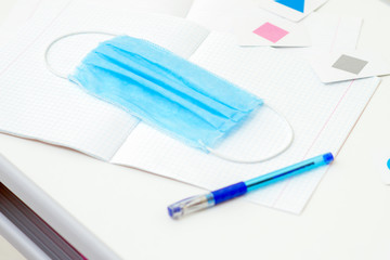 Naklejka premium Medical protective mask over copybook on the white desk. Home learning concept.