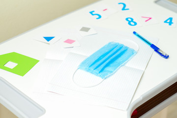 Medical protective mask and pen over copybook near numbers on the desk. Concept of primary school in quarantine.