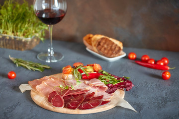 Assorted meat delicacies, cut into thin slices on a round wooden Board. Decorated with bruschetta with vegetables and fresh herbs