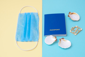 Travel concept during coronavirus. Travel and flight still life concept with a passport, medical mask and seashells on a blue and yellow background. Selective focus.