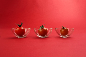 Red ripe cherry tomato with stem on red paper background copy text space mini glass bowl