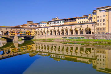 Fototapeta premium The famous Ponte Vecchio, the Old Bridge and city houses with reflections in the Arno River, Florence, Tuscany, Italy