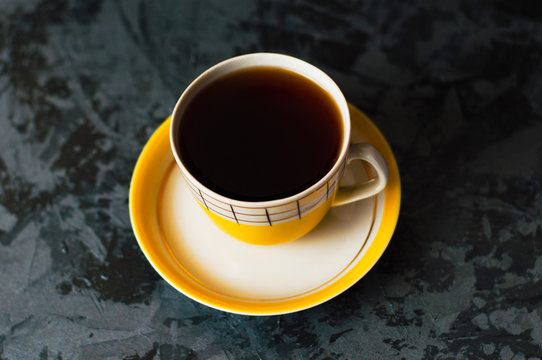 One yellow vintage cup with tea or coffee on a dark background