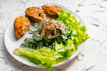 Colorful delicious dish with a salad of sorrel and sour cream, topped with fried sesame seeds, next to fried steaks of red fish pink salmon in breadcrumbs