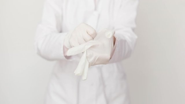 Female doctor or nurse in white coat putting on white protective rubber gloves. Close up, isolated on white background. Healthcare and medicine, hygiene and desease prevention concept