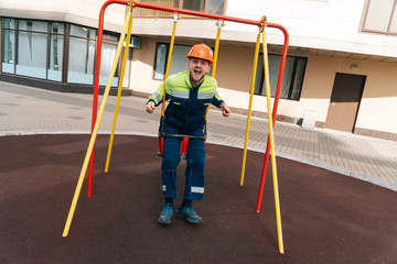 builder is swinging on swing at the playground of the future multi-story building. concept of riding an adult male on carousel