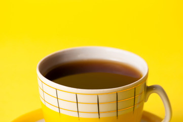 Yellow cup of tea or coffee without foam, close-up on a yellow background. Minimalistic composition with vintage subject and place for text.