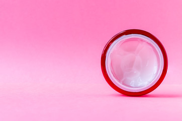 Round open red plastic jar with with white cream inside on a pink background with copy space. Skin care, cosmetics concept. Beauty packaging template. Side top view