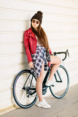 Fototapeta na wymiar Young girl riding a bike in a red jacket looks at camera lowering her glasses