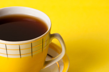 A yellow cup of tea or coffee without foam, close-up on a yellow background. Minimalistic composition with a vintage subject and place for text on the right.