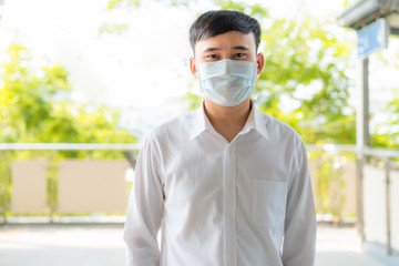 Young Asian businessman in white shirt going to work in pollution city she wears protection mask prevent PM2.5 dust, smog, air pollution and COVID-19 in Bangkok, Thailand.