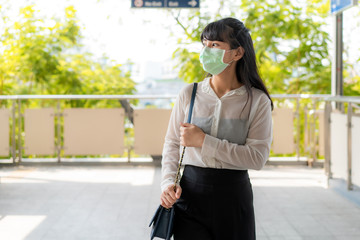 Young stress Asian businesswoman in white shirt going to work in pollution city she wears protection mask prevent PM2.5 dust, smog, air pollution and COVID-19 in Bangkok, Thailand.