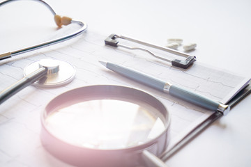 cardiogram with stethoscope, pen, magnifier, pills and glasses lay on a table