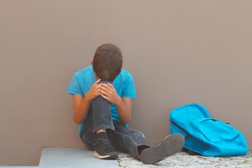 Sad child sitting alone near school on the ground outdoors