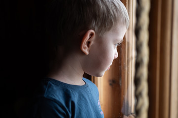 Sad little boy looking out of the window. 