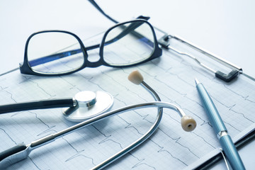 cardiogram with stethoscope, pen, magnifier, pills and glasses lay on a table