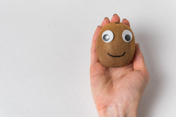 Hand holding kiwi with Googly eyes on white background. Products with funny faces