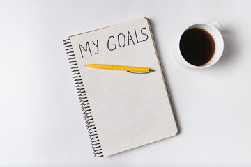 Fototapeta na wymiar Inscription in copybook MY GOALS. Cup of coffee and notepad. Top view