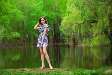 Fototapeta na wymiar Portrait of a young beautiful woman in blue dress posing by the lake