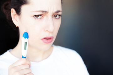 Young woman holding medicine equipment thermometer isolated on dark black background. Ill girl...
