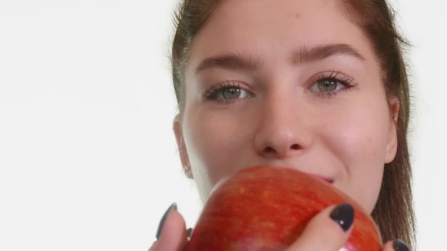 White girl bites red juicy apple on white background. Front view