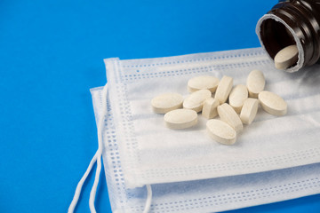White pills and medical protective masks on blue background. Text space