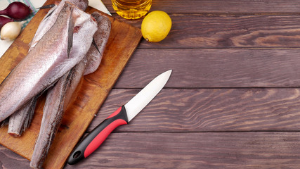 Three carcasses of fresh-frozen hake, pollock fish, on a cutting board on a wooden table. In the...
