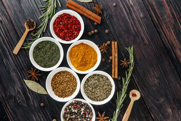 Flat displays of various spices in small white plates on a rustic wooden table.
