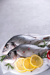 Delicious fresh fish on gray background. Fish with aromatic herbs, spices and lemon - healthy food, diet or cooking concept