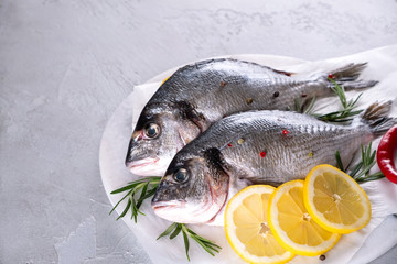 Fresh raw sea bream fish decorated with lemon slices, herbs on gray background. Healthy food concept, top view, copy space