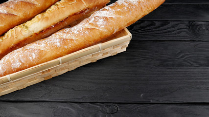 Different types of bread baguettes  in a wicker box on a black background. Place for text