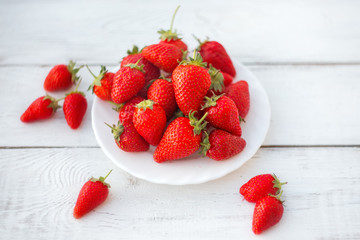 Delicious juicy strawberries on a white plate. Fresh strawberries close up on the white wooden background with copy space.