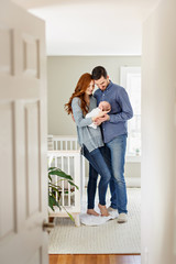 Happy parents admiring their newborn baby. Parents with a baby standing in freshly painted nursery.