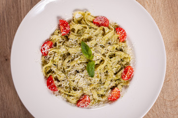  Plate with delicious tagliatelle pasta with pesto sauce, parmesan, cherry tomatoes and basil leafs on white plate. Top down view