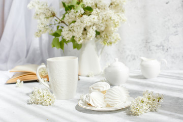 Still life vase with a bouquet of white lilac, a Cup of coffee with marshmallows, a plate of meringue, a sugar bowl and a milk jug , an old book. Postcard good morning.