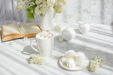 Still life vase with a bouquet of white lilac, a Cup of coffee with marshmallows, a plate of meringue, a sugar bowl and a milk jug , an old book. Postcard good morning.