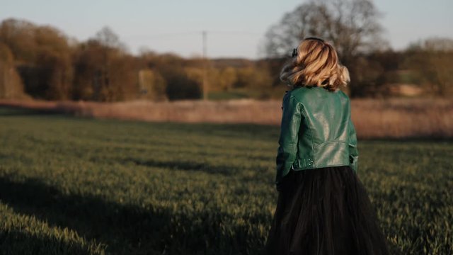 young woman in a long black dress and leather jacket running around in the field