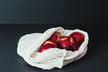 Fresh nectarines in string bag, shopper on the black background, zero waste concept, no plastic, reusable, eco friendly philosophy