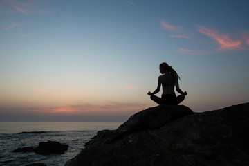 Yoga woman silhouette in Lotus position on the evening ocean.