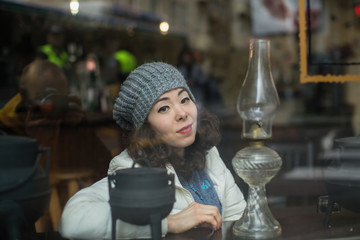 Asian woman posing for a photographer reflection in the glass, looks out from behind the cafeteria window.