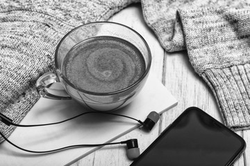Cup of hot coffee or hot Chocolate with earphones on rustic wooden table, closeup photo warm sweater with mug, winter morning concept, top view