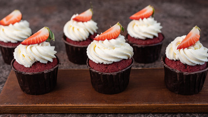 Red velvet cupcakes with white cream on top decorated with strawberry slice.