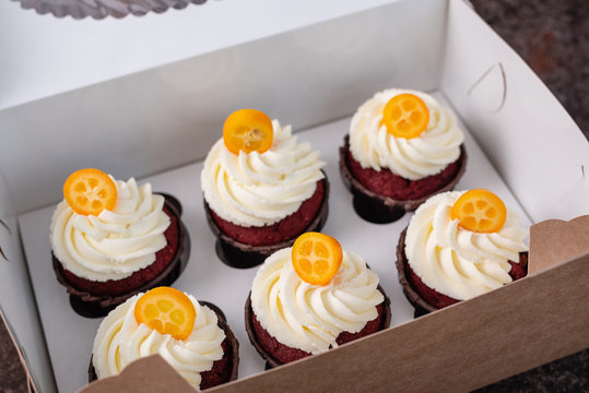 Red velvet cupcakes with white cream on top decorated with kumquat slice. Cupcakes in a box.